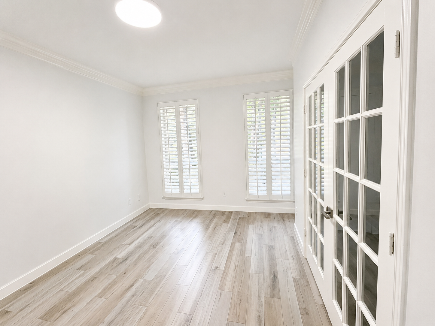 A bright, polished home office framed by glass-panel doors, plantation shutters, and wood-look tile flooring. A bright, polished home office framed by glass-panel doors, plantation shutters, and wood-look tile flooring.